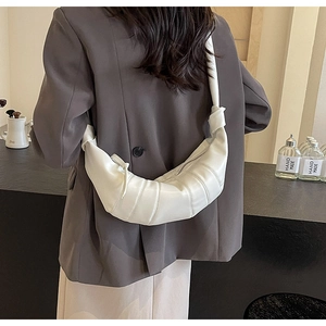 Close-up of white PU leather croissant bag with quilted pleats and knotted shoulder strap
