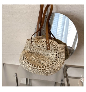 Detailed view of woven straw texture and brown leather handle with X-shaped stitching