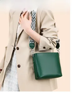 Detail of dark green pebble leather bucket bag featuring a woven geometric wide strap