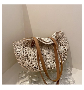 Detail of a semicircular straw tote bag showing beige weaving and brown leather handles