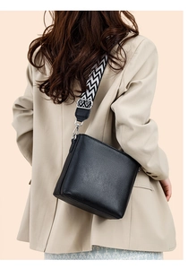 Detail of black lychee leather bucket bag with geometric patterned wide strap on a model