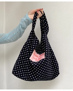 Detail showing white polka dot pattern on black canvas tote with pink fabric label