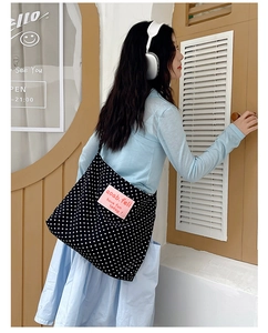 Detail of black canvas tote bag with white polka dots and pink rectangular label