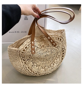 Detailed view of semi-circular straw tote with brown leather handles and X-stitch sewing