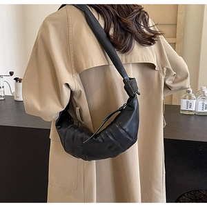 Detail of black pleated PU leather croissant bag with knotted strap on casual trench coat