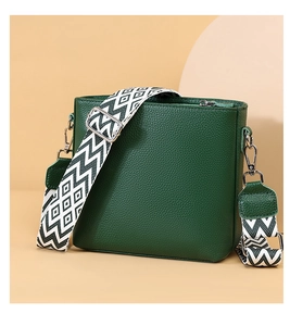 Detail of green litchi grain leather bag featuring a wide geometric woven shoulder strap