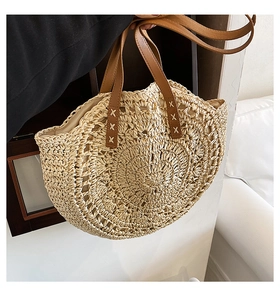 Detail of hand-woven straw bag showing brown leather handle with white X-stitch detail
