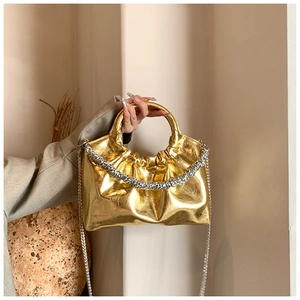 Close-up of gold PU handbag with pleated texture and sparkling silver chain strap