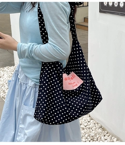 Detail showing the large capacity black polka dot canvas tote bag worn by a model