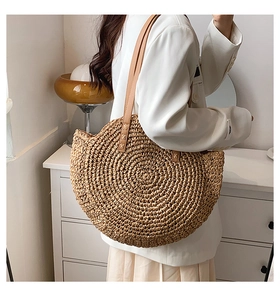 Detail of a semi-circular straw shoulder bag featuring textured weaving and leather straps