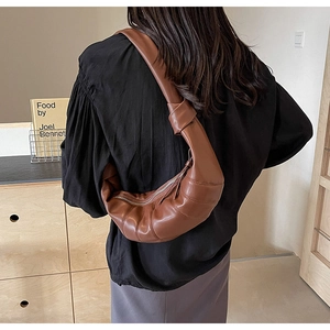 Brown PU leather croissant bag featuring pleated texture and wide knotted shoulder strap