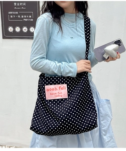 Detailed close-up of large canvas crossbody bag with white polka dots and pink logo label