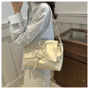Detail of cream white tote bag with cross ribbon and bow decoration on the flap