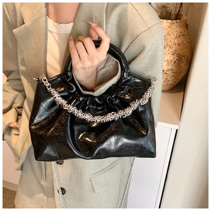Detail of glossy black PU leather cloud bag with silver textured chain and thin strap
