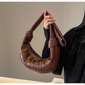 Detail of a dark brown croissant bag with quilted design and polished PU material