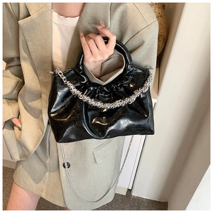 Detail of black pleated cloud bag with silver chain worn over a green suit jacket