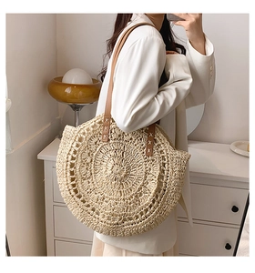 Detailed view of the spiral straw texture and brown leather handles on a summer woven tote bag