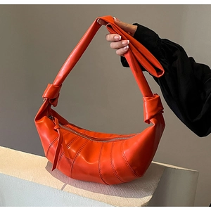 Close-up of bright orange PU leather croissant bag with knotted strap and zipper detail