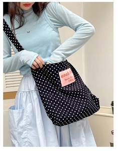 Detailed view of polka dot canvas tote bag with pink label and lettering on shoulder