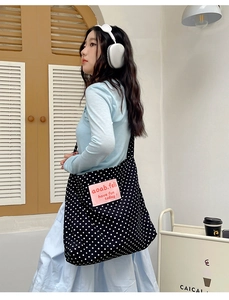 Detail view of black canvas tote bag with white polka dots and pink logo label