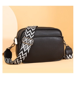 Détail du sac bandoulière en cuir noir avec texture litchi et sangle tissée géométrique