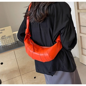 Detail view of quilted croissant shoulder bag in bright orange PU leather on female model