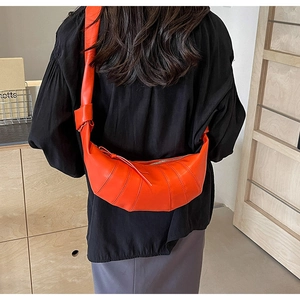 Crossbody view of bright orange croissant bag with spiral quilting and knotted strap