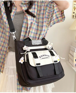 Detail of a nylon crossbody bag with rubber brand patch and cute cartoon doll pendant