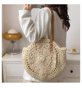 Detail of a large round straw tote bag featuring radial weave and brown leather shoulder straps