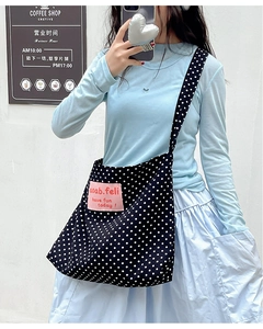 Close-up of black canvas crossbody bag with white polka dots and pink logo patch detail