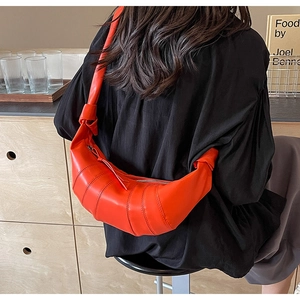 Detail of an orange PU leather crescent bag with pleated stitching and knot strap