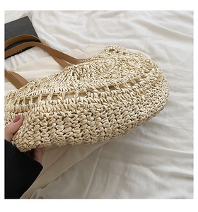 Detail shot of the hollow woven texture and brown leather handles on the straw bag