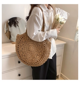 Detail view of large straw tote bag with brown leather strap worn by a female model