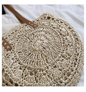 Detail of round straw bag showing beige woven texture and brown leather handle with X-stitching