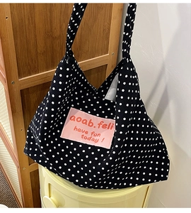 Close-up of black polka dot canvas tote bag with pink patch detail and slogan