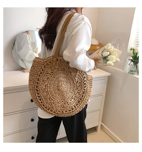 Detail view of a natural straw woven semicircular shoulder bag with brown leather straps