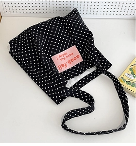 Detail view of black canvas bag with white polka dots and a pink fabric label design