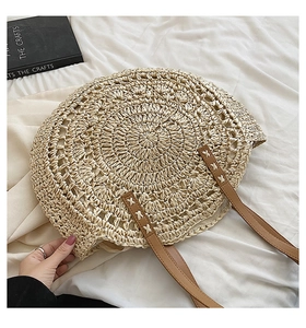 Detail of hand-woven round straw bag featuring intricate cutout patterns and leather straps