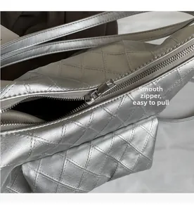 Close-up of smooth metal zipper and quilted diamond pattern on silver handbag