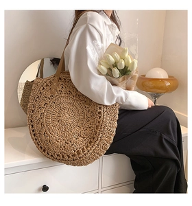 Lifestyle shot of a large round straw woven tote bag with brown leather straps