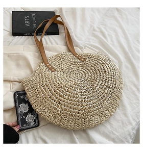 Detail of the circular woven straw tote bag featuring brown leather handles and spiral texture