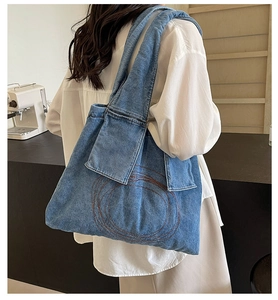 Detail of blue denim tote bag with brown ring embroidery and pockets on the shoulder strap
