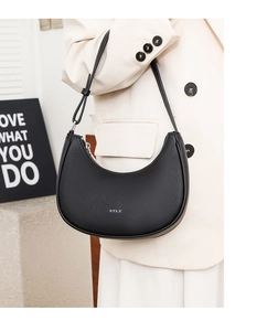 Close-up of black pebble leather moon bag featuring silver STLY logo and sleek metal zipper