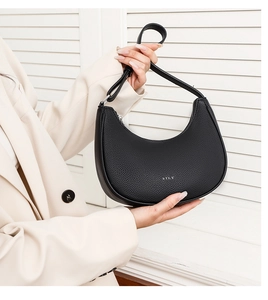 Detail of black pebbled leather hobo bag with silver STLY logo held by a model in a suit