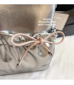 Close-up of metallic silver shoulder bag featuring a cute pink leather bowknot and metal charms