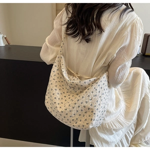 Close-up of a floral canvas tote bag shown on a model wearing a white dress in a cozy room