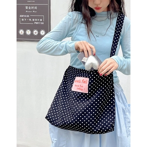 Casual black canvas crossbody bag with white polka dots and pink logo patch on a model