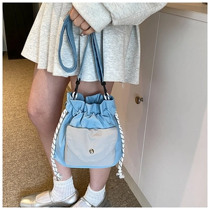 Detailed view of light blue oxford crossbody bucket bag with drawstring and front pocket
