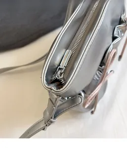 Detail view of smooth silver PU leather crossbody bag featuring top zipper and pink ribbon