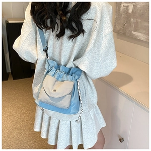 Detail of light blue nylon drawstring crossbody bag with front pocket shown in daily use